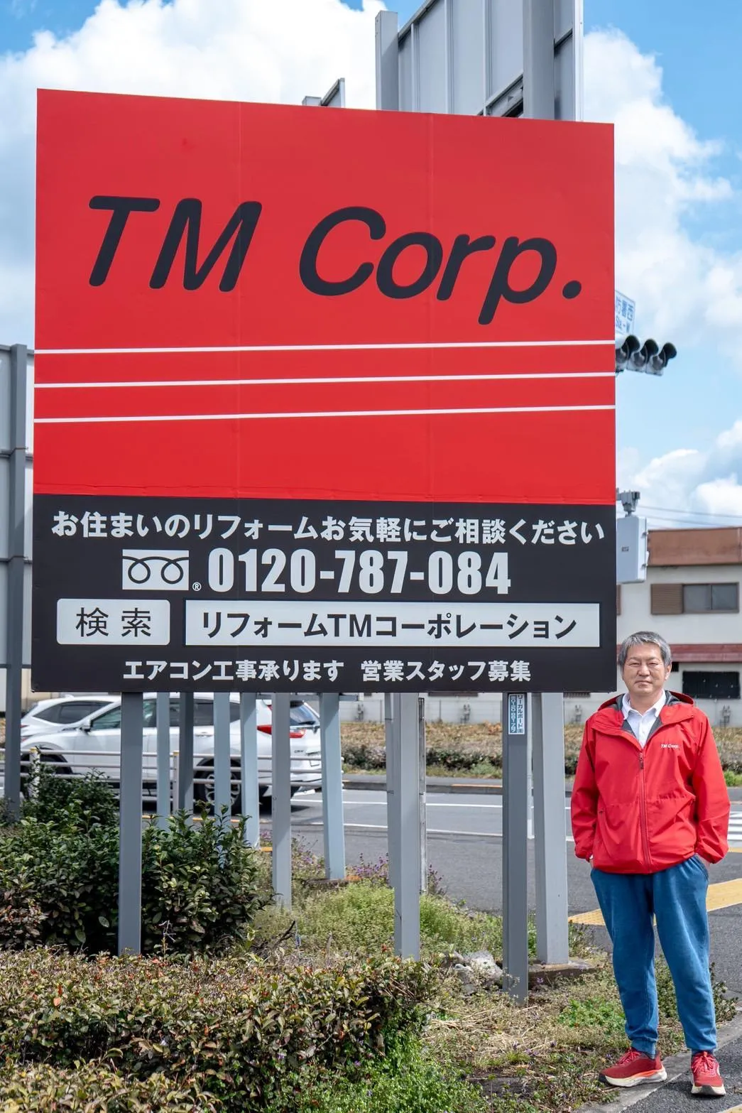 株式会社TMコーポレーションの看板前に立つ代表取締役 青木 徹